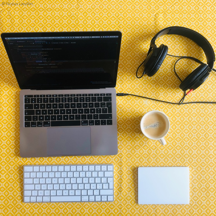 Une table avec un ordinateur, un clavier externe, un casque et un café